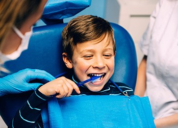 Child smiling while brushing teeth in treatment chair