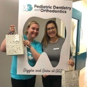 Dental team member and two young twins with my first dental appointment sign