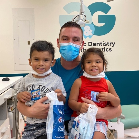 Doctor Cory smiling with two young dental patients