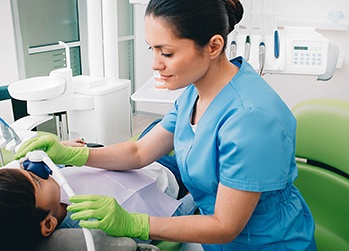 Woman in blue scrubs and green gloves removing nitrous oxide mask from boy’s nose