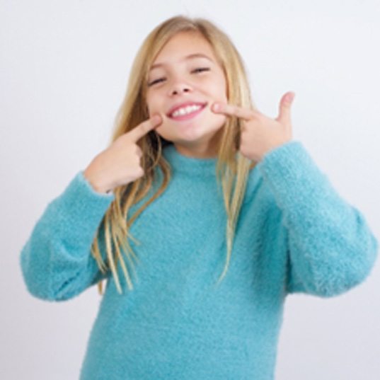 Child with straight teeth pointing to her smile