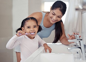 Mother and daughter smiling while brushing teeth in bathroom