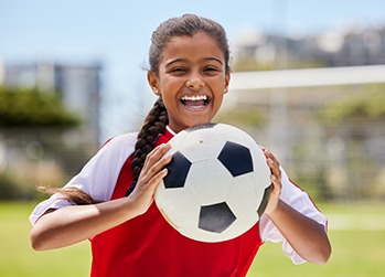 Smiling child holding soccer ball on field