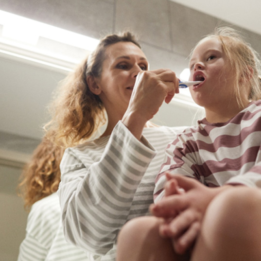 Mom helping daughter brush her teeth at home 