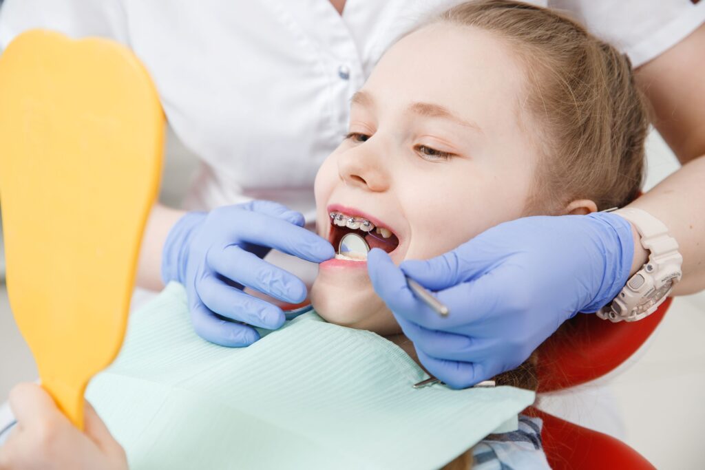 Girl with braces holding mirror as dentist works on her teeth
