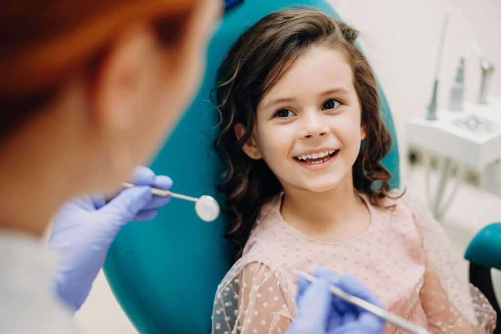 Girl in teal dental chair smiling at dentist before exam