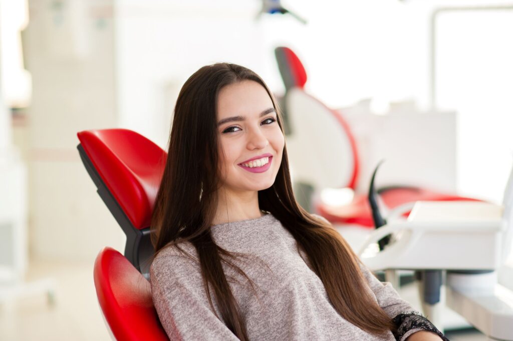 Young woman sitting in red dental chair smiling