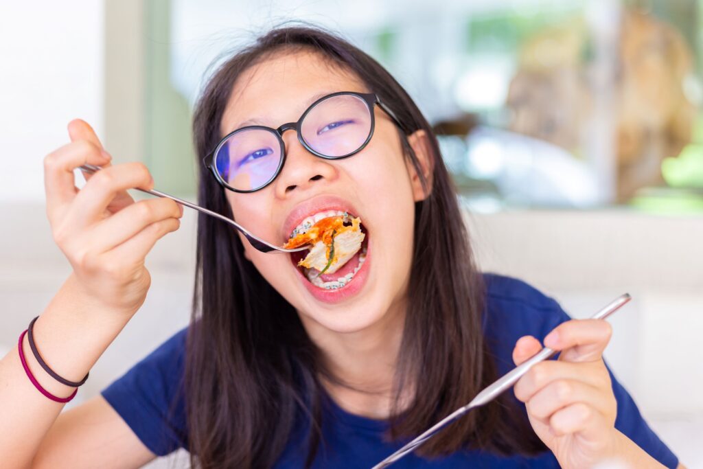 Girl in blue shirt and braces eating pizza with utensils