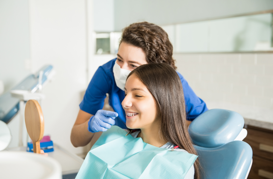 Teen in dental chair looking at mirror while dentist looks on